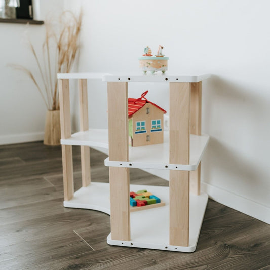 Unser MODURA Eckregal steht im Kinderzimmer vor einer weißen Wand. Das Bild ist so fotografiert worden, dass man sowohl die geölten Seitenplanken als auch die drei weißen Ablagen gut erkennen kann. In den Fächern sind Spielsachen angeordnet.