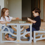var:grau-lernturm-hocker / var:grau-lernturm-rutsche-hocker / Zwei Geschwisterkinder sitzen gemeinsam am zum Kindertisch umgebauten grauen Lernturm im Baum-Design und spielen Memory.
