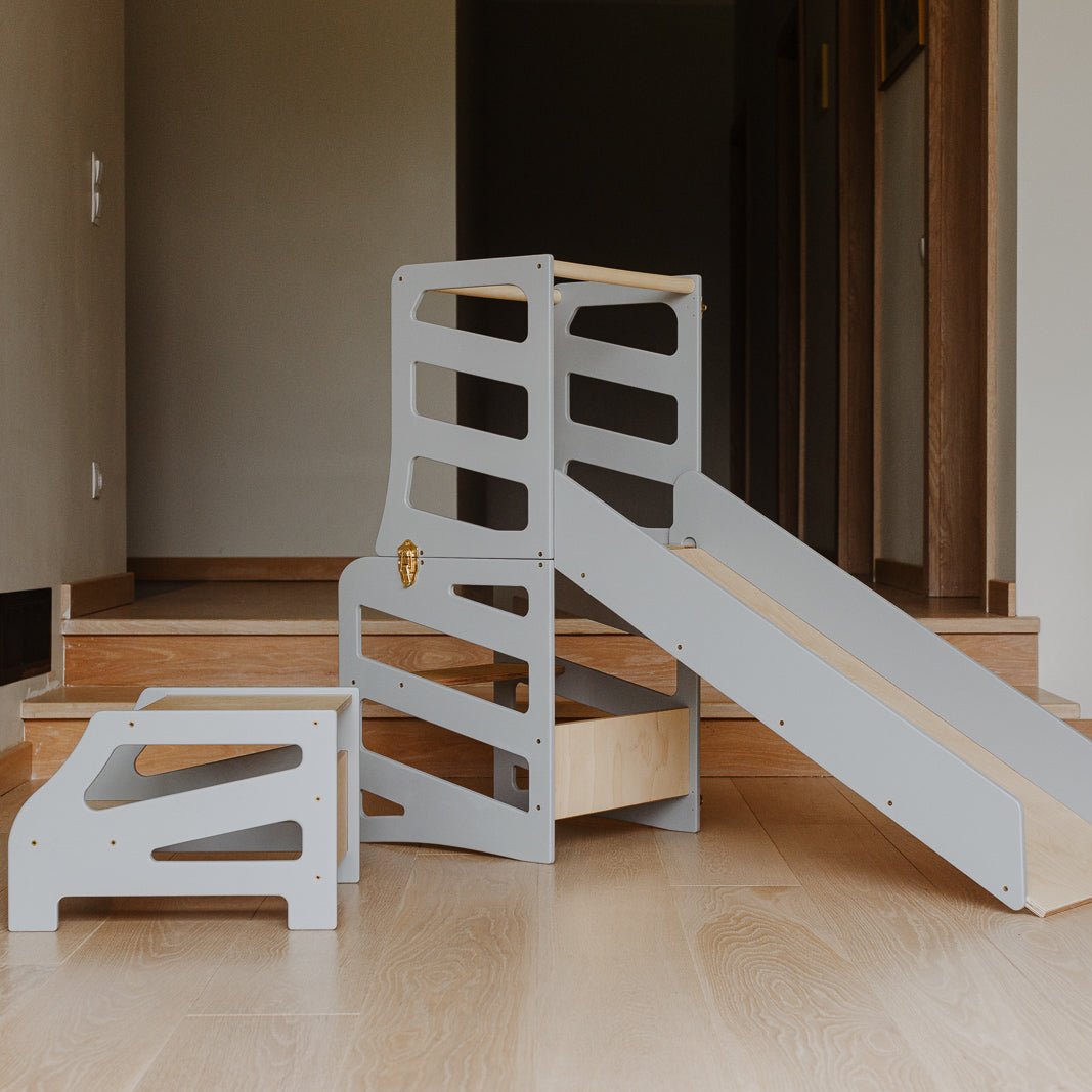 var:grau-lernturm-rutsche-hocker / Der graue Lernturm mit Tischfunktion im Streifen-Design inklusive Rutsche und Extra-Hocker im Fokus.