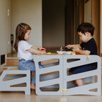 var:grau-lernturm-hocker / var:grau-lernturm-rutsche-hocker / Zum Kindertisch umgebauter, grauer Lernturm inklusive Extra-Hocker mit zwei spielenden Kindern.