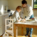var:weiß-lernturm / var:weiß-lernturm-rutsche / var:weiß-lernturm-hocker / var:weiß-lernturm-rutsche-hocker / Ein Kleinkind backt mit sdeinem Vater einen Kuchen während es auf der Plattform des weißen Lernturmes steht.