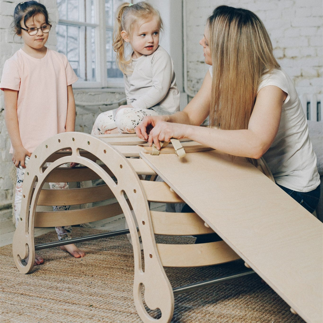 Eine Mutter redet mit ihren Kindern, die gerade mit einem XXL Kletterbogen mit Rutsche spielen.