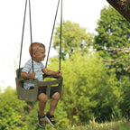 Ein Kleinkind schwingt fröhlich im Freien in der geschützten Schaukel in grau.