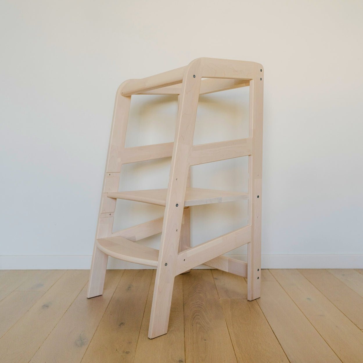 Der Lernturm aus Massivholz ohne montiertem Rausfallschutz steht vor einer weißen Wand auf einem Holzboden mit Dielen.