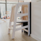 Der geschützte Lernturm aus Massivholz von der Seite fotografiert vor einer schwarzen Küchentheke. 