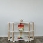 das Eckregal steht mittig im Kinderzimmer vor einer weißen Wand. Ausführung mit 3 Ablagen in weiß + klares Öl.