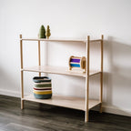 Die Midi-Variante des ISKORA Holzregales für Kinderzimmer & Wohnräume mit drei Regalböden angelehnt an einer weißen Wand. Spielzeug und ein Korb aus Stoff sind darin angeordnet.