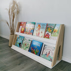 Kinderbücherregal nach Montessori als Teil eines modularen Regalsystemes steht einzeln vor einer weißen Wand im Kinderzimmer. Ablagen sind weiß lackiert, Seitenteile geölt.