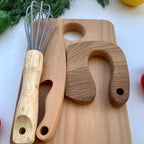 Nahaufnahme eines Montessori Küchensets. Man sieht ein Frühstücksbrett auf dem ein Schneidemesser, ein Kindermesser und ein Schneebesen nach Montessori liegen.