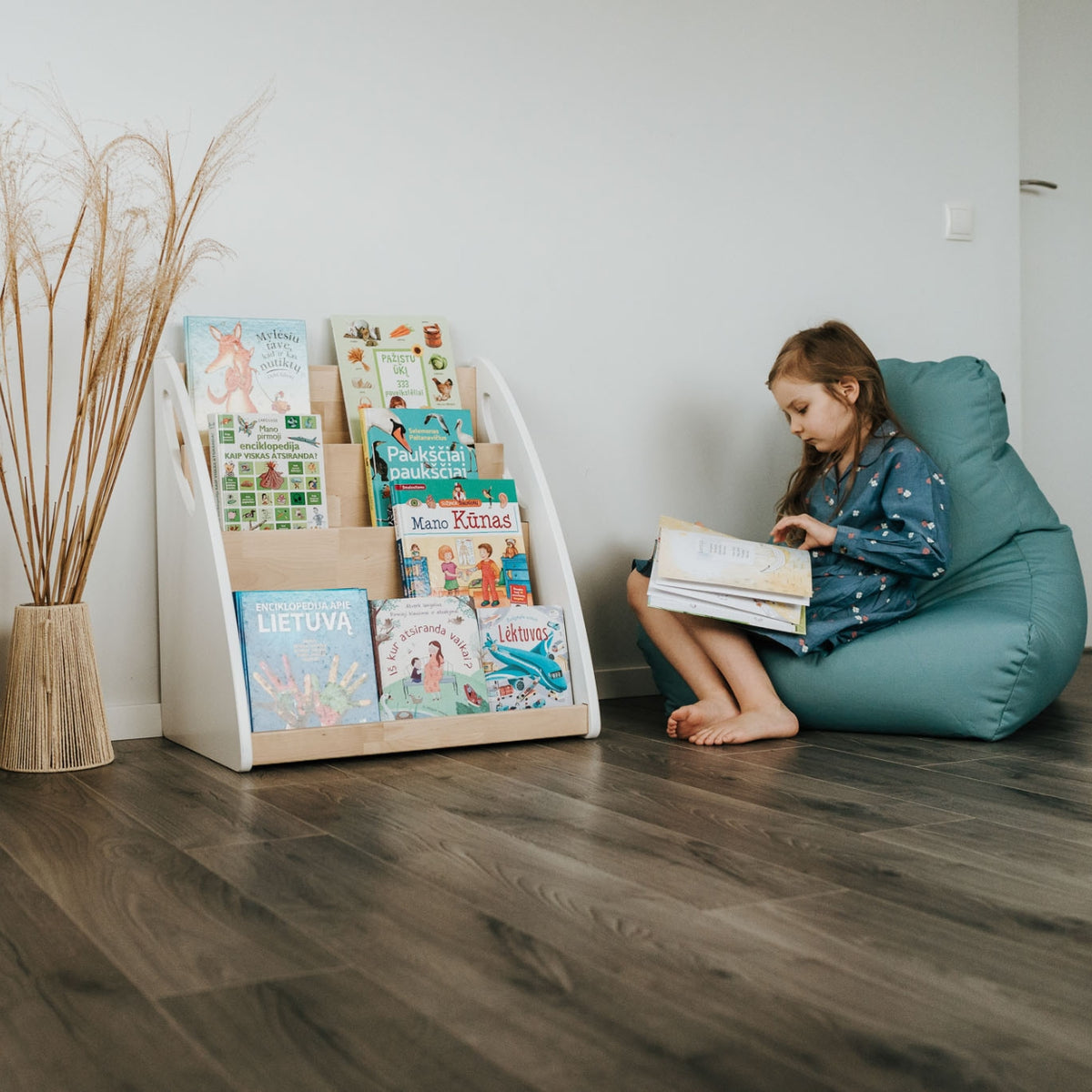 Ein Mädchen sitzt auf einem Sitzsack neben einem Montessori Bücherregal und blättert konzentriert in einem Buch.