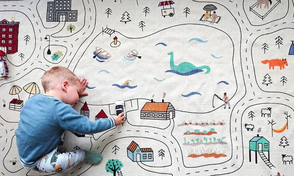 Ein Kind spielt mit Autos auf den Straßen des Spielteppichs "Entdecker".