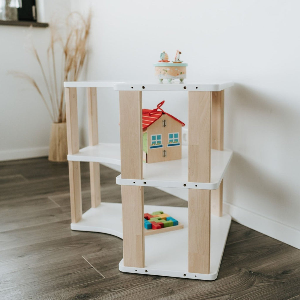 Unser MODURA Eckregal steht im Kinderzimmer vor einer weißen Wand. Das Bild ist so fotografiert worden, dass man sowohl die geölten Seitenplanken als auch die drei weißen Ablagen gut erkennen kann. In den Fächern sind Spielsachen angeordnet.