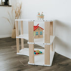 Unser MODURA Eckregal steht im Kinderzimmer vor einer weißen Wand. Das Bild ist so fotografiert worden, dass man sowohl die geölten Seitenplanken als auch die drei weißen Ablagen gut erkennen kann. In den Fächern sind Spielsachen angeordnet.